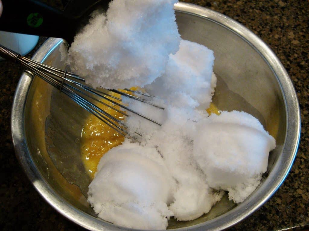 Scoops of freshly fallen snow added to other ingredients in a metal bowl.