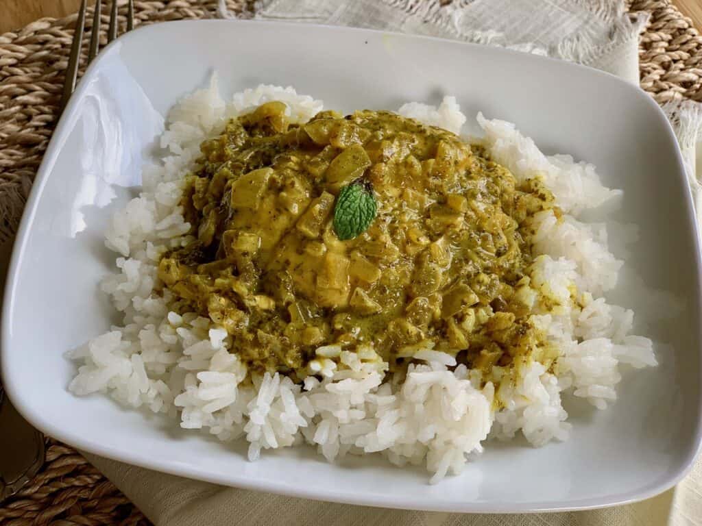 Slow-Cooked Green Chicken Masala is served over rice and garnished with a mint leaf.