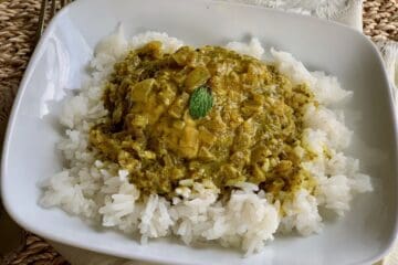 Slow-Cooked Green Chicken Masala is served over rice and garnished with a mint leaf.