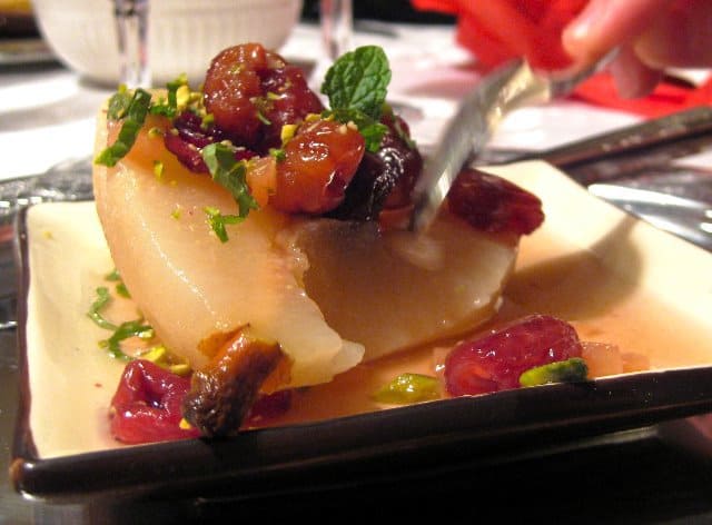 Poached Pears filled with marinated red fruit and topped with chopped mint served being eaten with a spoon.