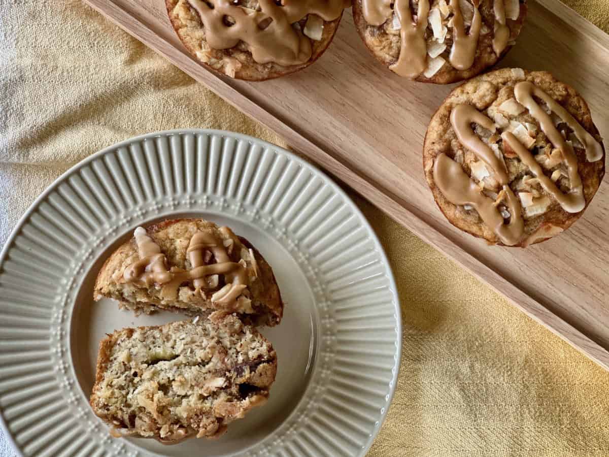 A Java Monkey Muffin cut in half to reveal its inner texture, beside a tray of whole muffins. 