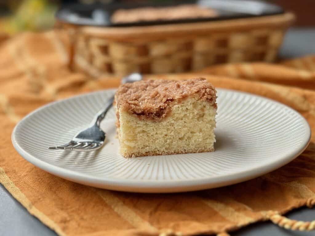 A slice of Cinnamon Coffee Cake served on a plate beside a basket.