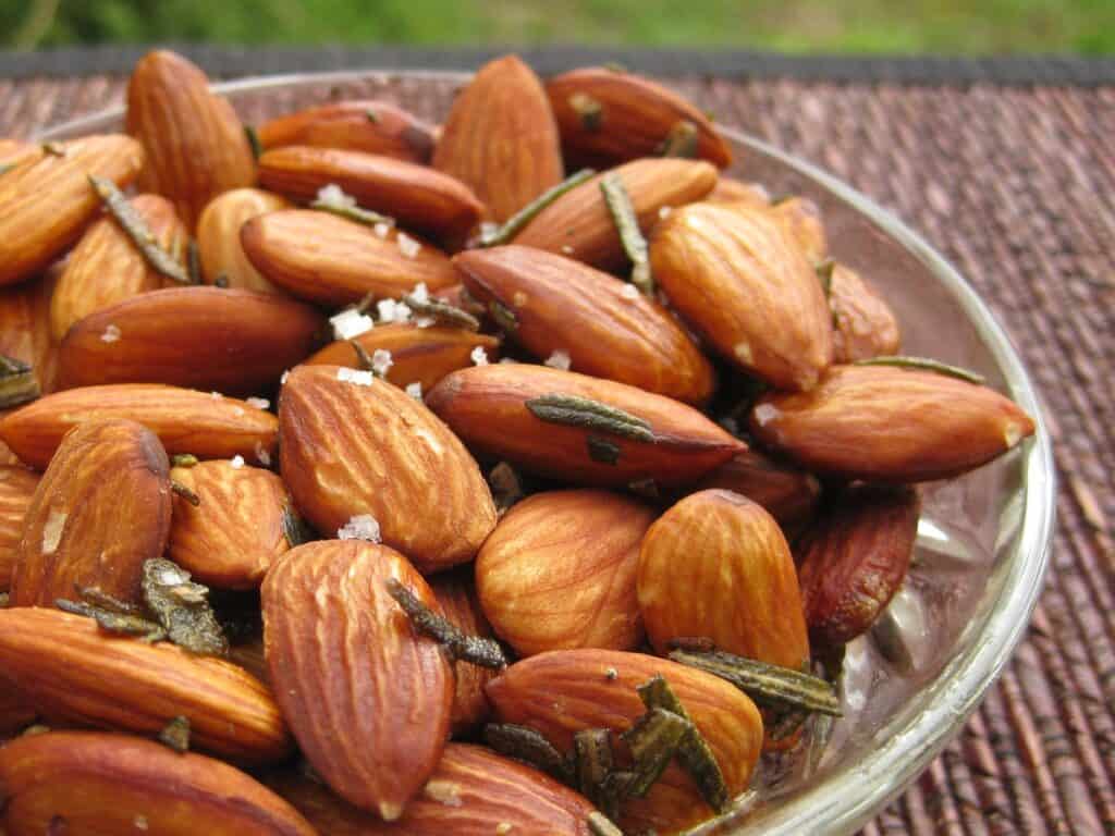 Fried almonds with rosemary buts and sea salt in a small glass serving dish.