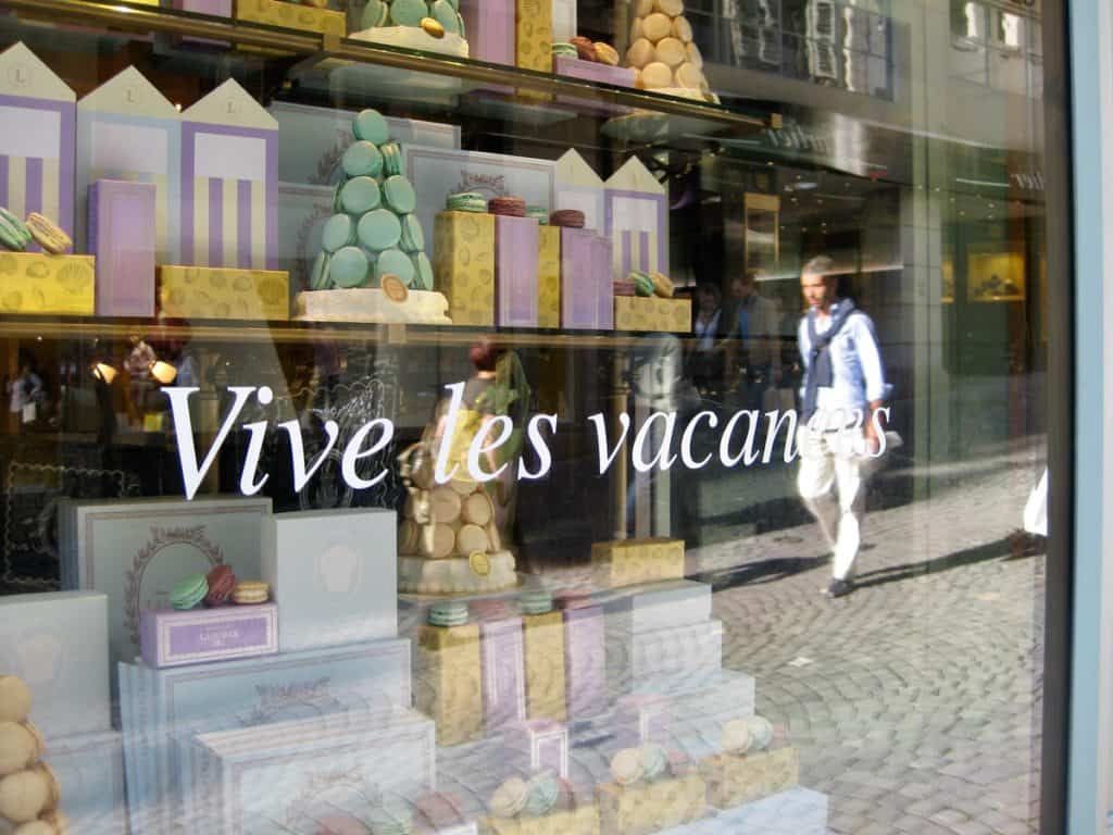 A reflection in the window of a shop displaying macarons along a cobblestone street in Lausanne, Switzerland.