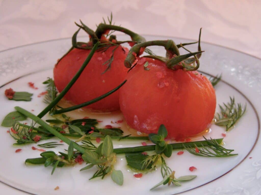 Stemmed Tomatoes Stuffed with Goat Cheese are arranged on a plate scattered with fresh herbs.