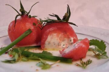 Tomatoes Stuffed with Goat Cheese are sliced open to reveal the filling on a small plate.