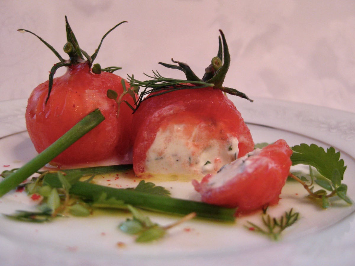 Tomatoes Stuffed with Goat Cheese are sliced open to reveal the filling on a small plate.