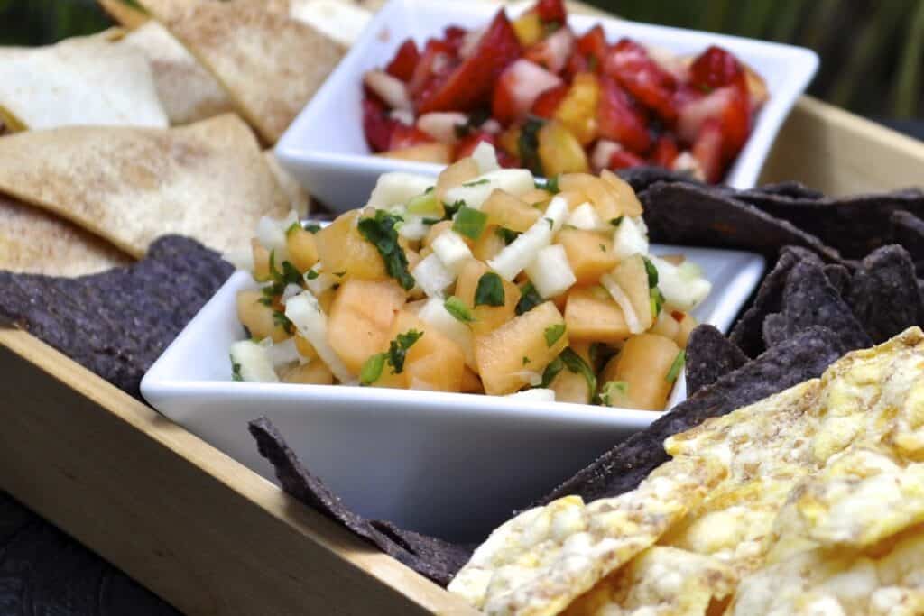 Sweet Strawberry Salsa and Cantaloupe Salsa are both served with crispy chips on a wooden tray.