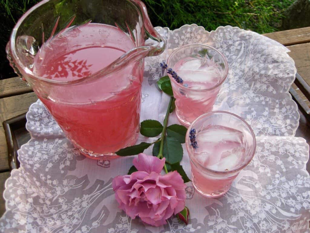 A pitcher of Lavender Lemonade beside two filled glasses and a lavender rose.
