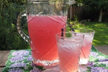 A pitcher of Lavender Lemonade and two full glasses on an antique floral cloth.