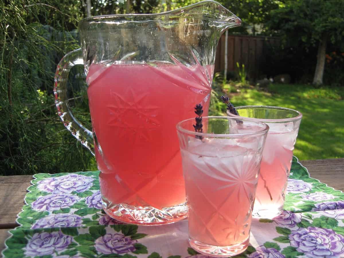 A pitcher of Lavender Lemonade and two full glasses on an antique floral cloth.