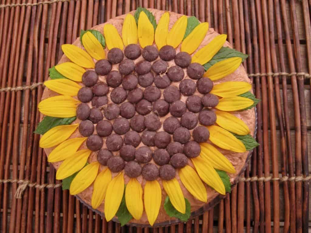 A Sunflower Cake on a glass platter sitting on a stick mat in the garden, viewed from above.