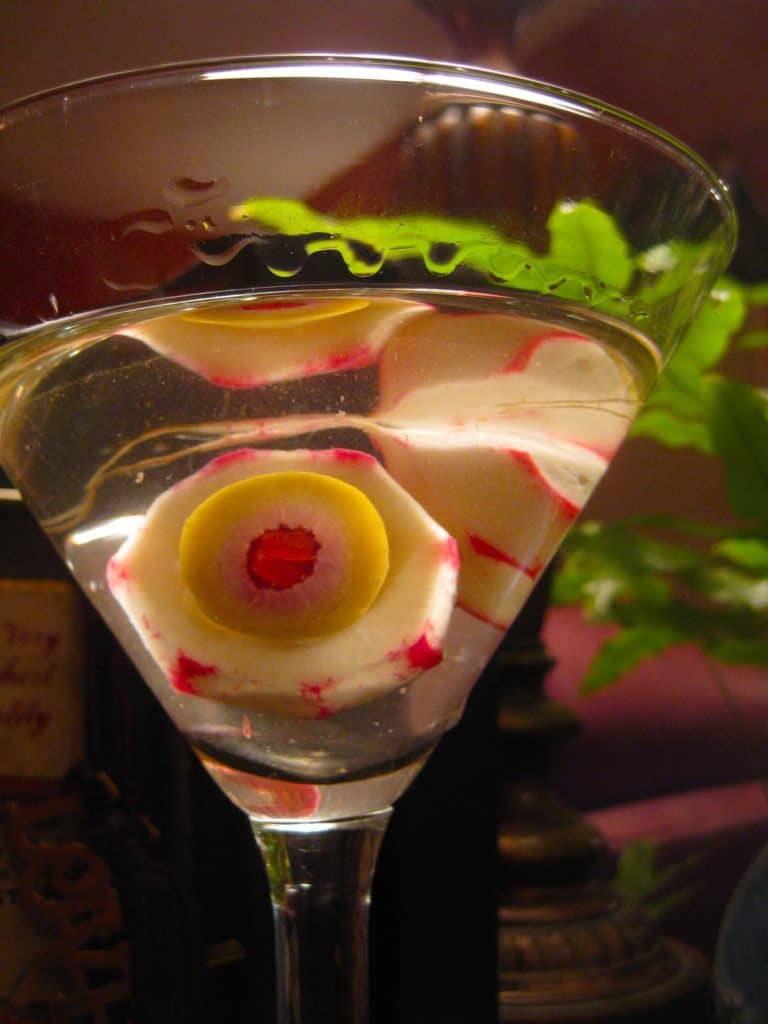 Cocktail Eyeballs made from radishes and olives look spooky suspended in a clear drink in a martini glass.