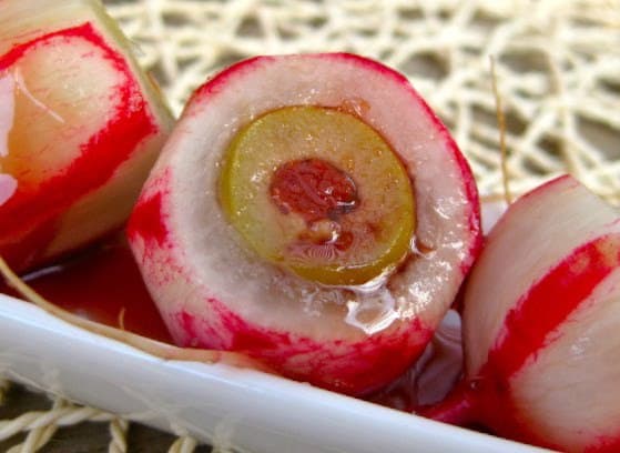 A Cocktail Eyeball drizzled with pomegranate dressing and served as an appetizer on an olive tray.