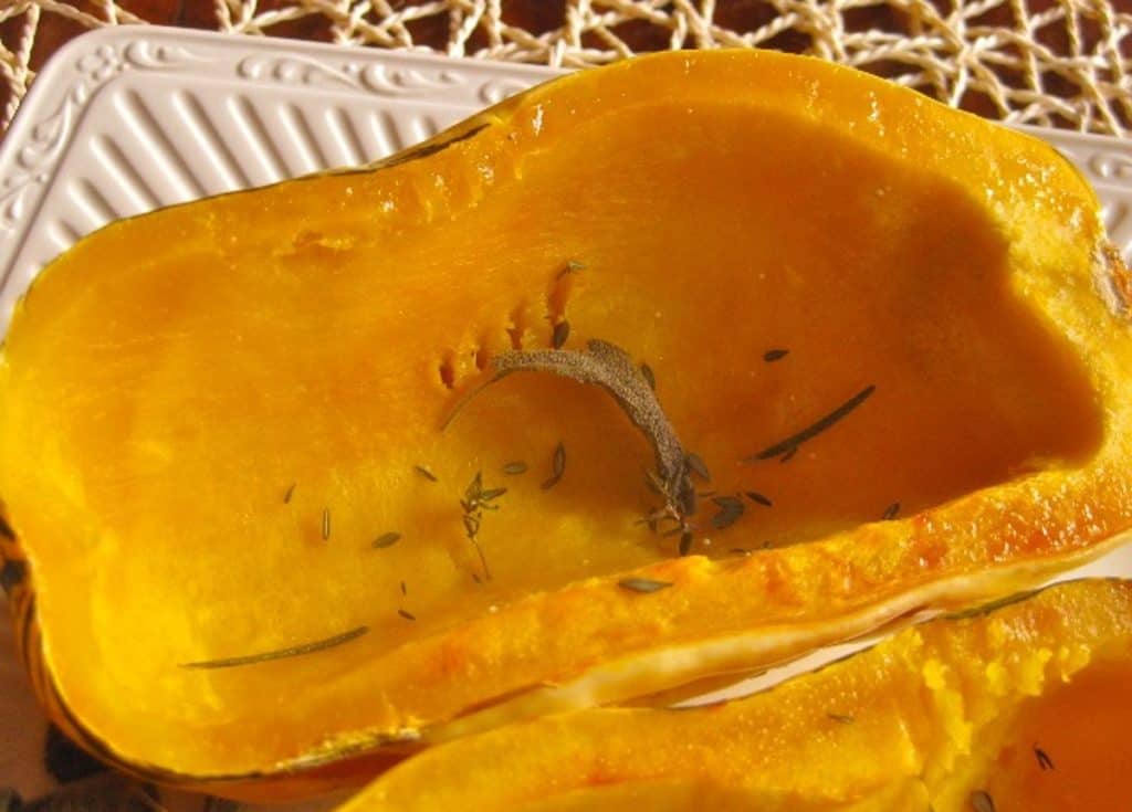 Roasted Delicata Squash half with sage leaf on a white plate.