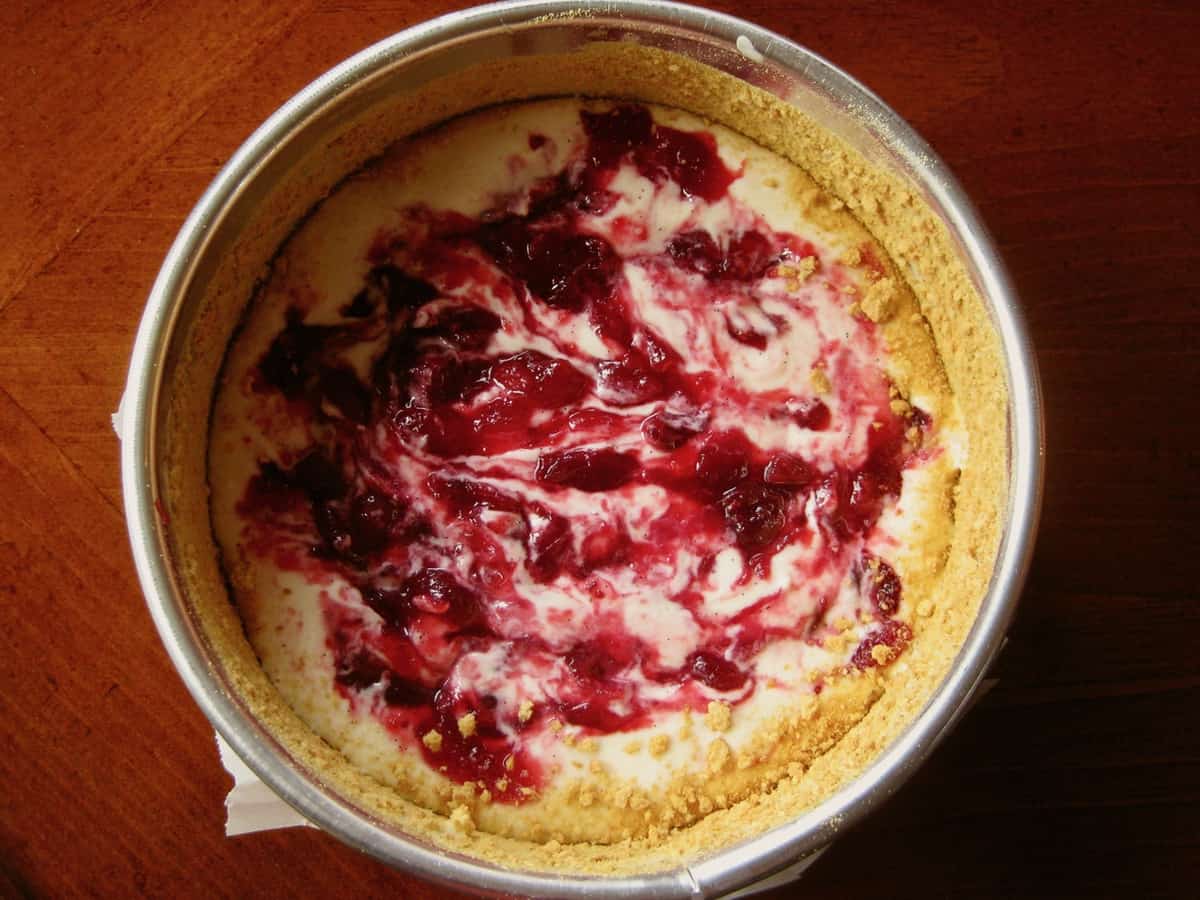 Cranberry Cheesecake Spread batter in a 6-inch springform pan marbled with cranberry sauce before baking.