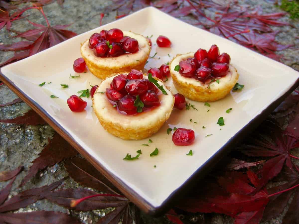 Pomegranate Goat Cheese Tarts on a square plate surrounded by autumn leaves.