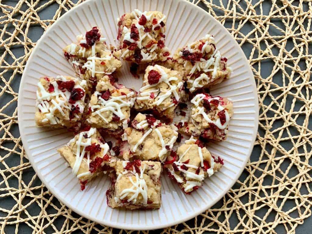 Cranberry Pecan Cookies with White Chocolate Drizzle and Cranberry Bits served on a white plate displayed on a woven mat. 