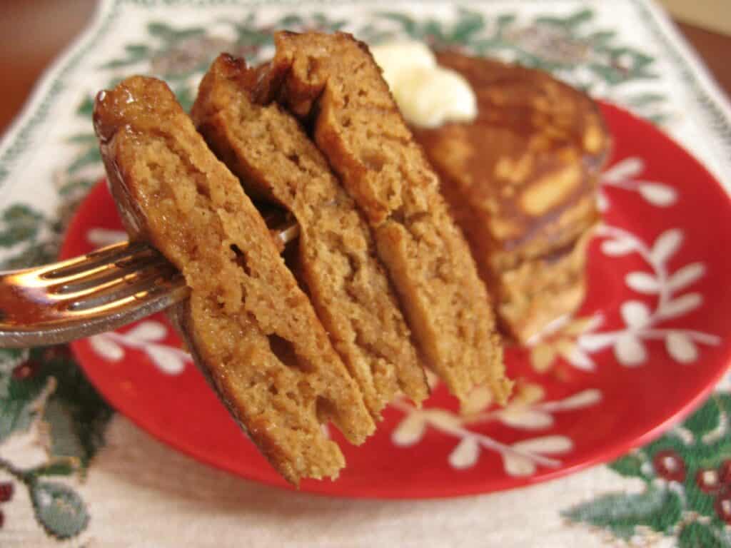 A fork full of Gingerbread Pancakes with a plate of Pancakes in the background.