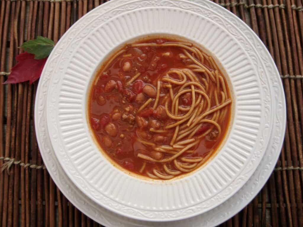 Kentucky Chili, or Bluegrass Chili, with pieces of spaghetti in the broth, is served in a shallow white bowl.