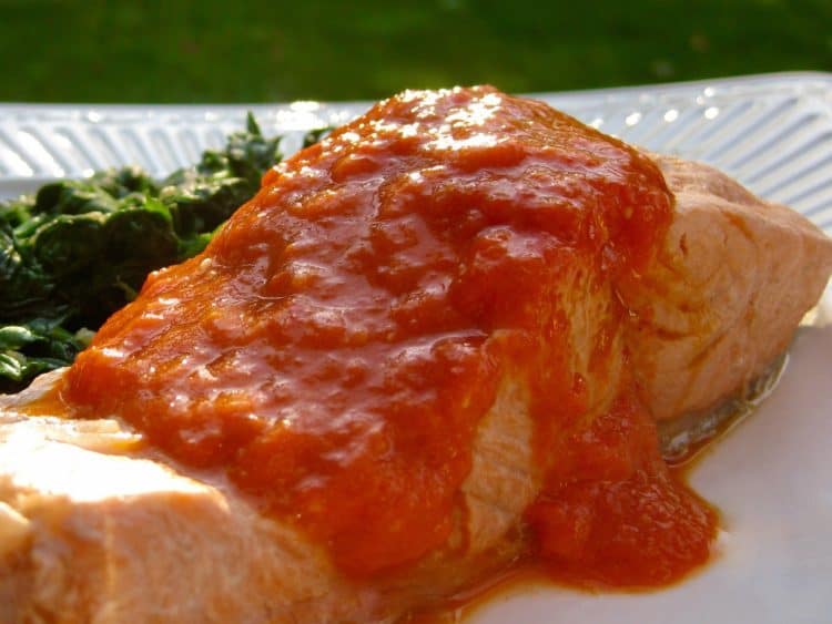 Pan Simmered Salmon topped with Roasted Red Pepper Sauce served on a white plate.