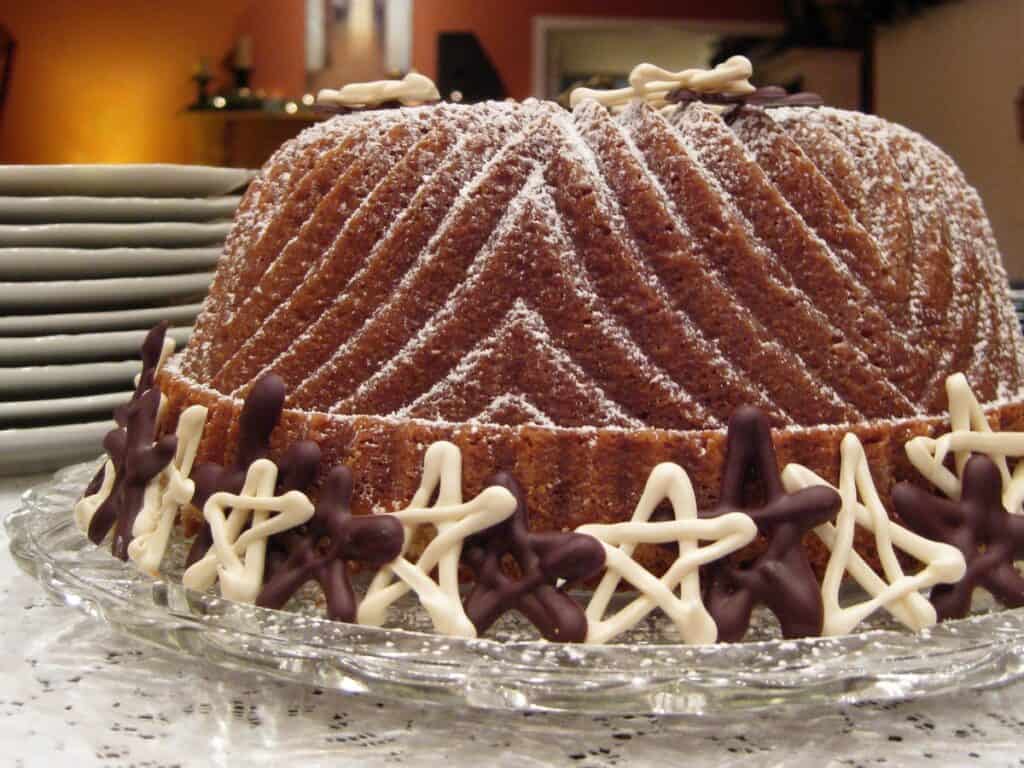 A Twelfth Night Cake dusted with powdered sugar and decorated with white and dark chocolate stars, beside a stack of dessert plates. 