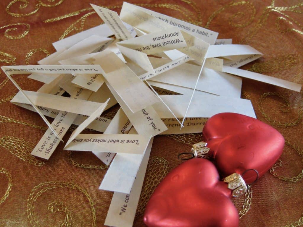 A pile of personalized fortunes are printed on folded strips of paper beside heart shaped ornaments.