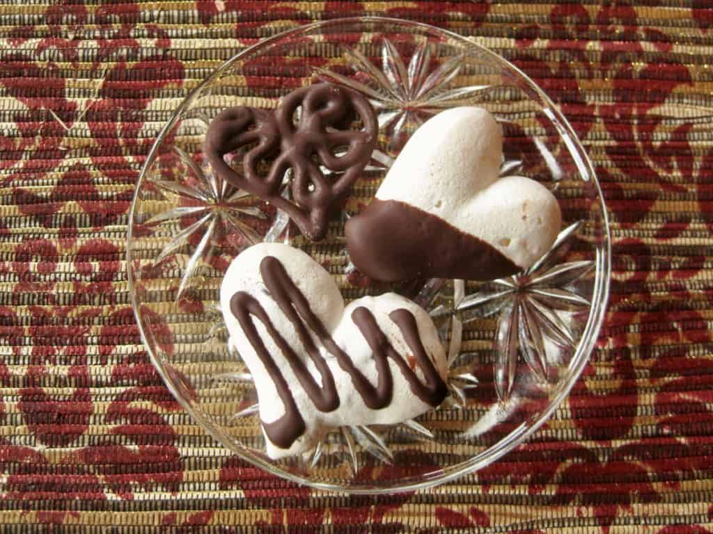 Valentine Meringue Cookie Hearts are dipped in chocolate or drizzled with chocolate and served on a small glass plate.