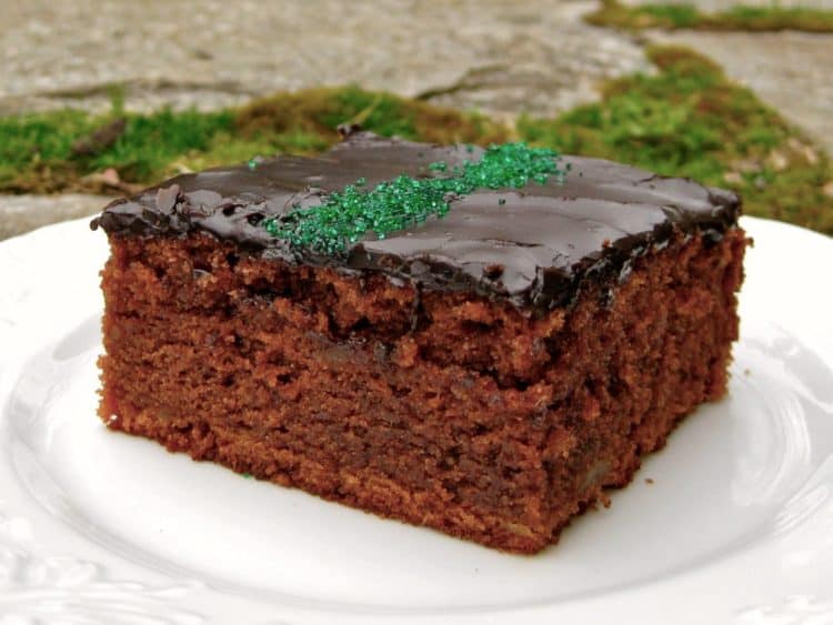 A square of Chocolate Potato Cake with Pour-over Frosting on a white plate set in the garden.