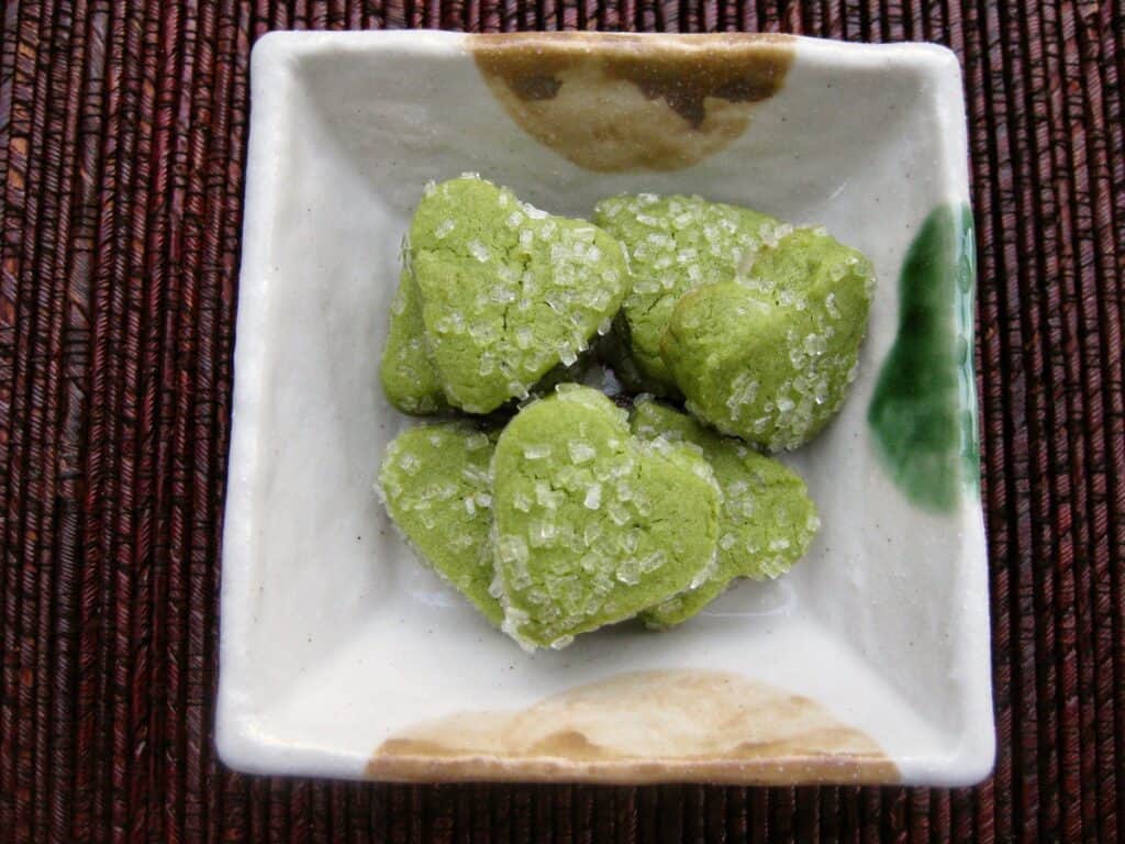 Tiny heart-shaped Green Tea Cookies (Matcha Shortbread) are served in a square Japanese dish.
