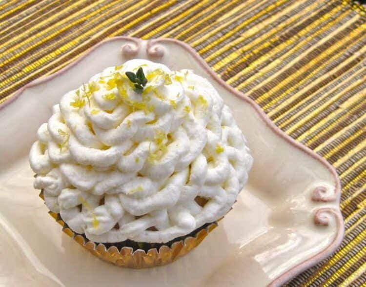 A Lemon Olive Oil Cupcake frosted with a swirl of Balsamic Whipped Cream, sprinkled with lemon zest and garnished with a sprig of lemon thyme.