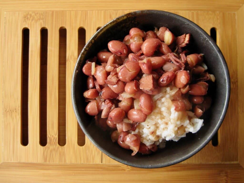 Red Beans ladled over rice in a rustic black bowl set on a wooden tray.