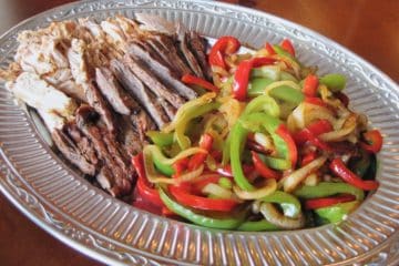 Sliced red and green bell peppers sautéed with onions are arranged on a platter with beef and chicken to make fajitas.