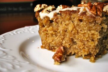 A slice of Old Fashioned Oatmeal Cake topped with Maple Glaze and toasted nuts is served on a white dessert plate.
