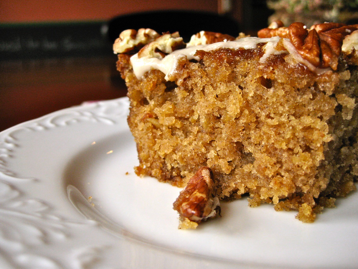 A slice of Old Fashioned Oatmeal Cake topped with Maple Glaze and toasted nuts is served on a white dessert plate.