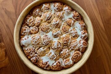 Quick and Easy Cinnamon Rolls drizzled with Orange Icing in a baking dish on a wooden table.