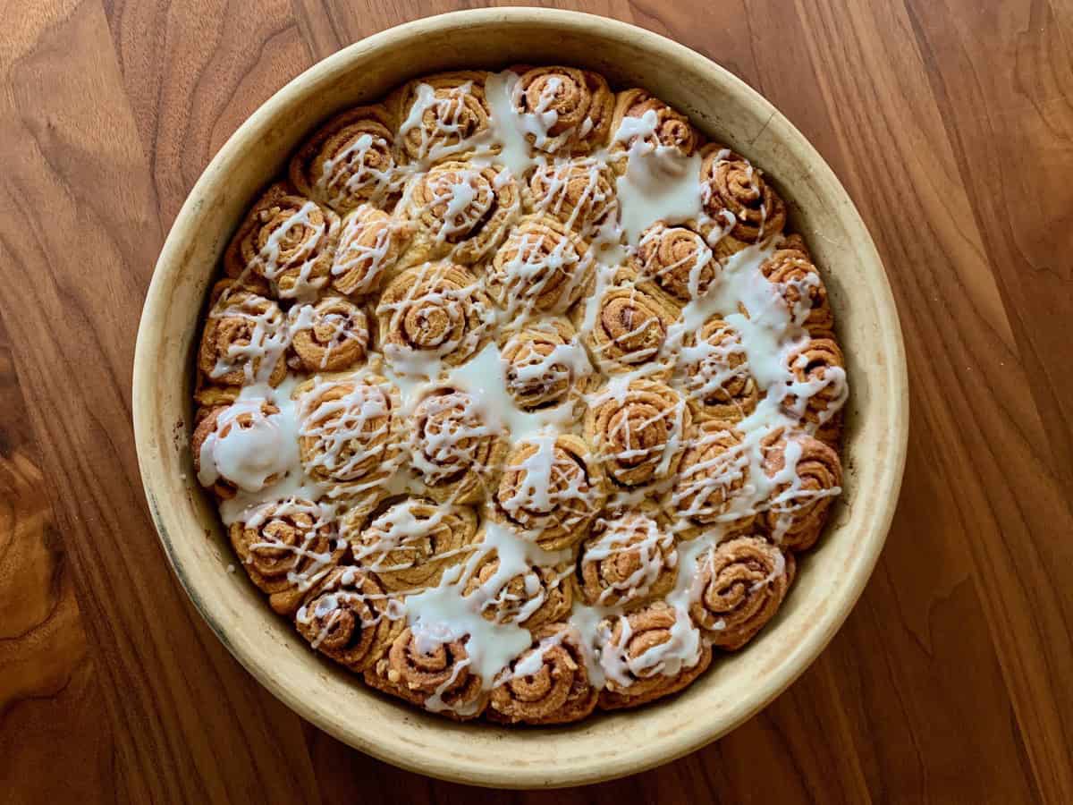 Quick and Easy Cinnamon Rolls drizzled with Orange Icing in a baking dish on a wooden table.