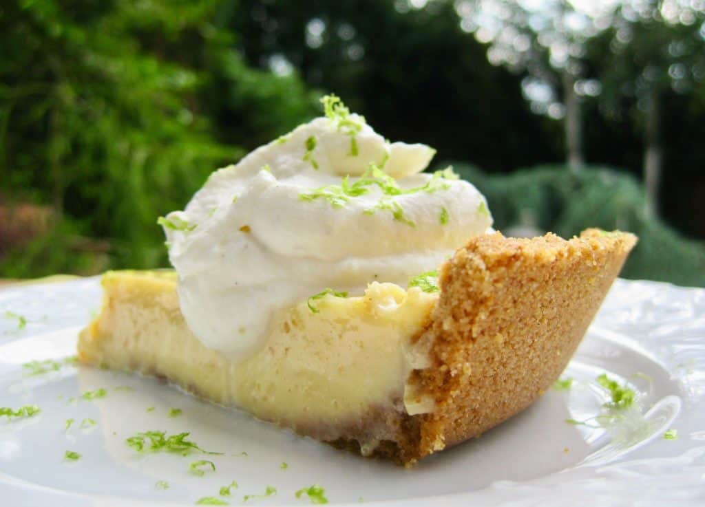 A slice of Key Lime Pie garnished with Whipped Cream and lime zest in a cardamom flavored graham cracker crust