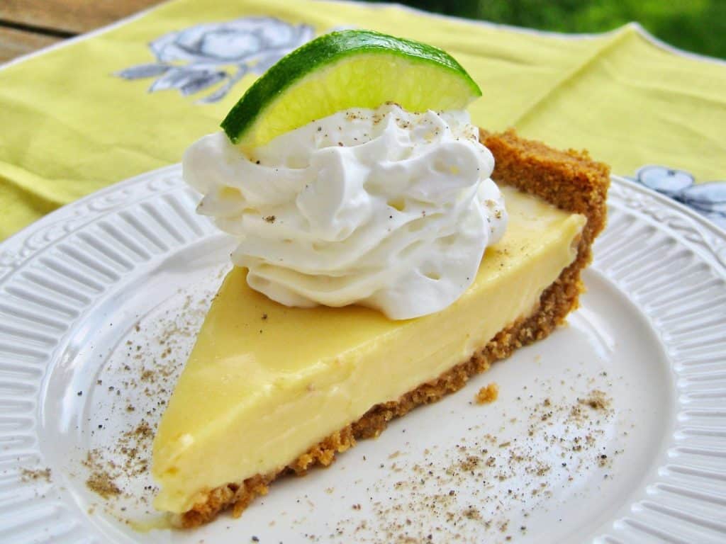 A slice of Key Lime Pie garnished with Whipped Cream and a slice of lime then dusted with cardamom