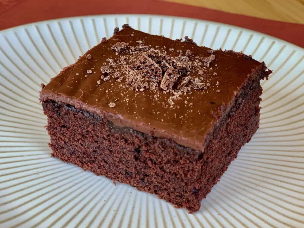 A square of Bishop Chocolate Cake with Fudgy Icing served on a white plate.