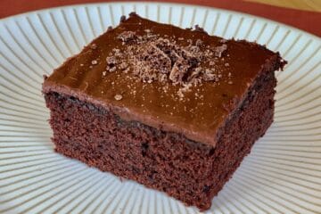 A square of Bishop Chocolate Cake with Fudgy Icing served on a white plate.