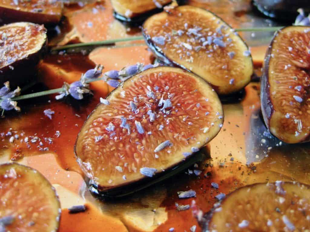 Halved figs drizzled with honey and dusted with lavender blossoms on a baking sheet.