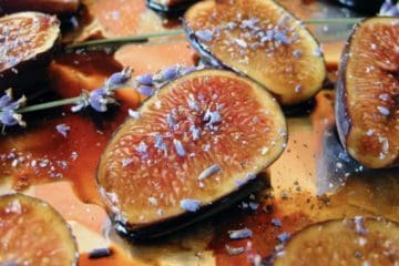 Halved figs drizzled with honey and dusted with lavender blossoms on a baking sheet.