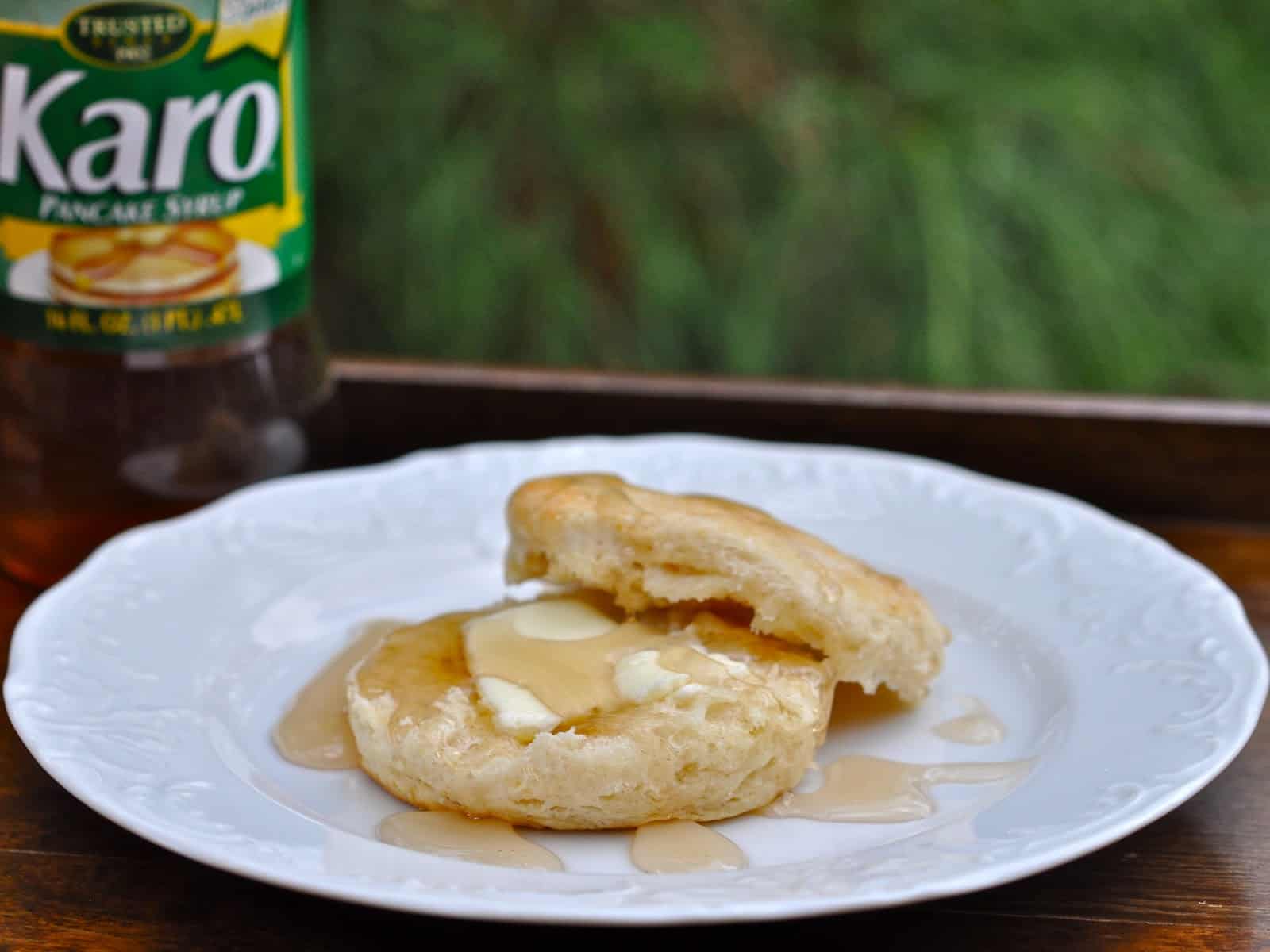 One of Uncle Hal's Biscuits Split and served on a plate with a smear of butter and drizzled with Karo syrup.