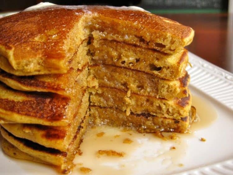 A stack of Pumpkin Pancakes featuring five pancakes, and a cutaway view inside the stack, drizzled with maple syrup.