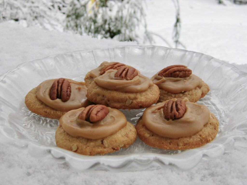 Pecan Praline Cookies with Brown Sugar Frosting served on a glass plate and resting on a snowy ledge.