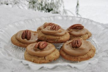 Pecan Praline Cookies with Brown Sugar Frosting served on a glass plate and resting on a snowy ledge.