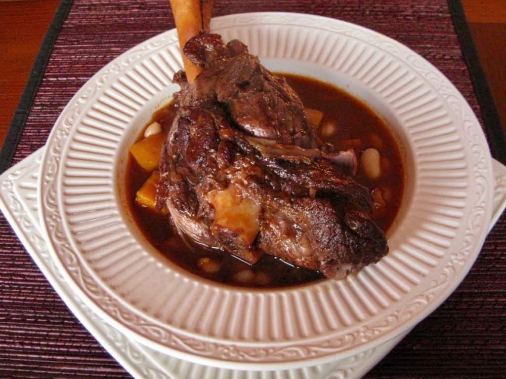 a hearty lamb shank braised in wine with squash and white beans, served in a shallow bowl