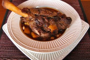 a tender braised lamb shank served in a shallow bowl over squash and white beans.