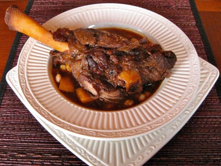 a tender braised lamb shank served in a shallow bowl over squash and white beans.